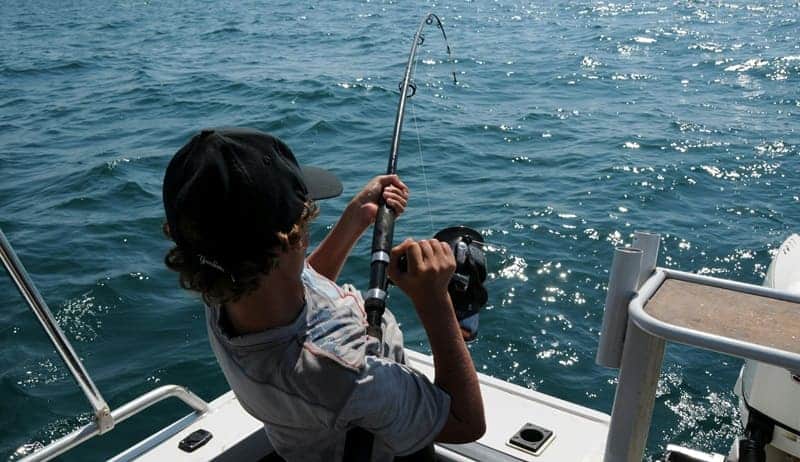 Young angler actively reels in a catch while on a boat